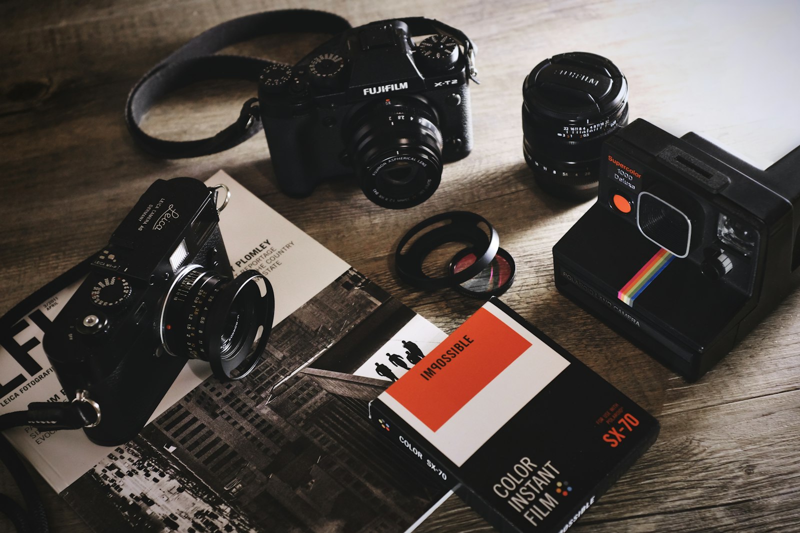 flat lay of cameras, a lens, and instant film accessories on a wooden surface