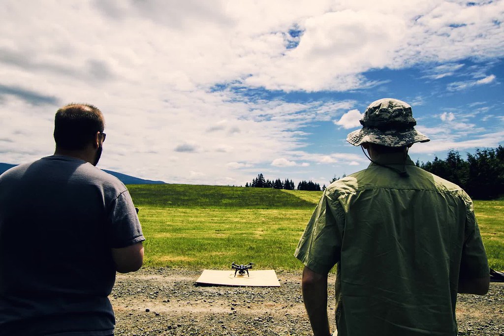 two people operating a drone in an open grassy field under a partly cloudy sky