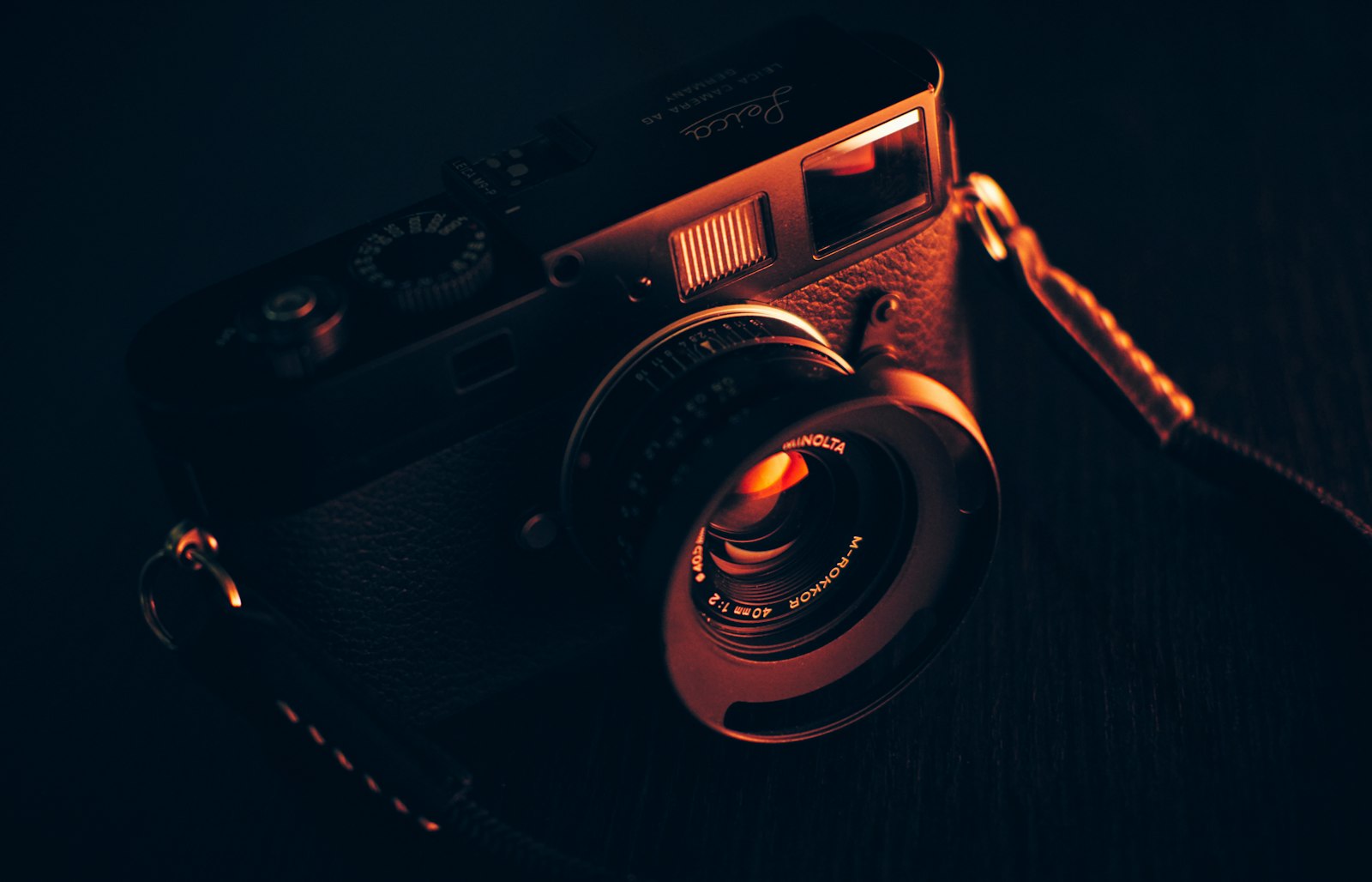 rangefinder-style camera with lens resting on a dark wooden table in warm light