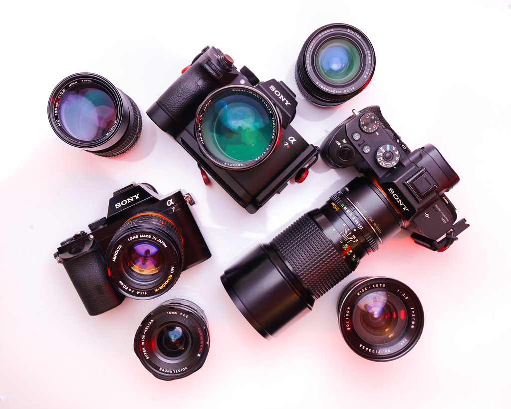 modern mirrorless cameras and assorted lenses arranged on a white surface