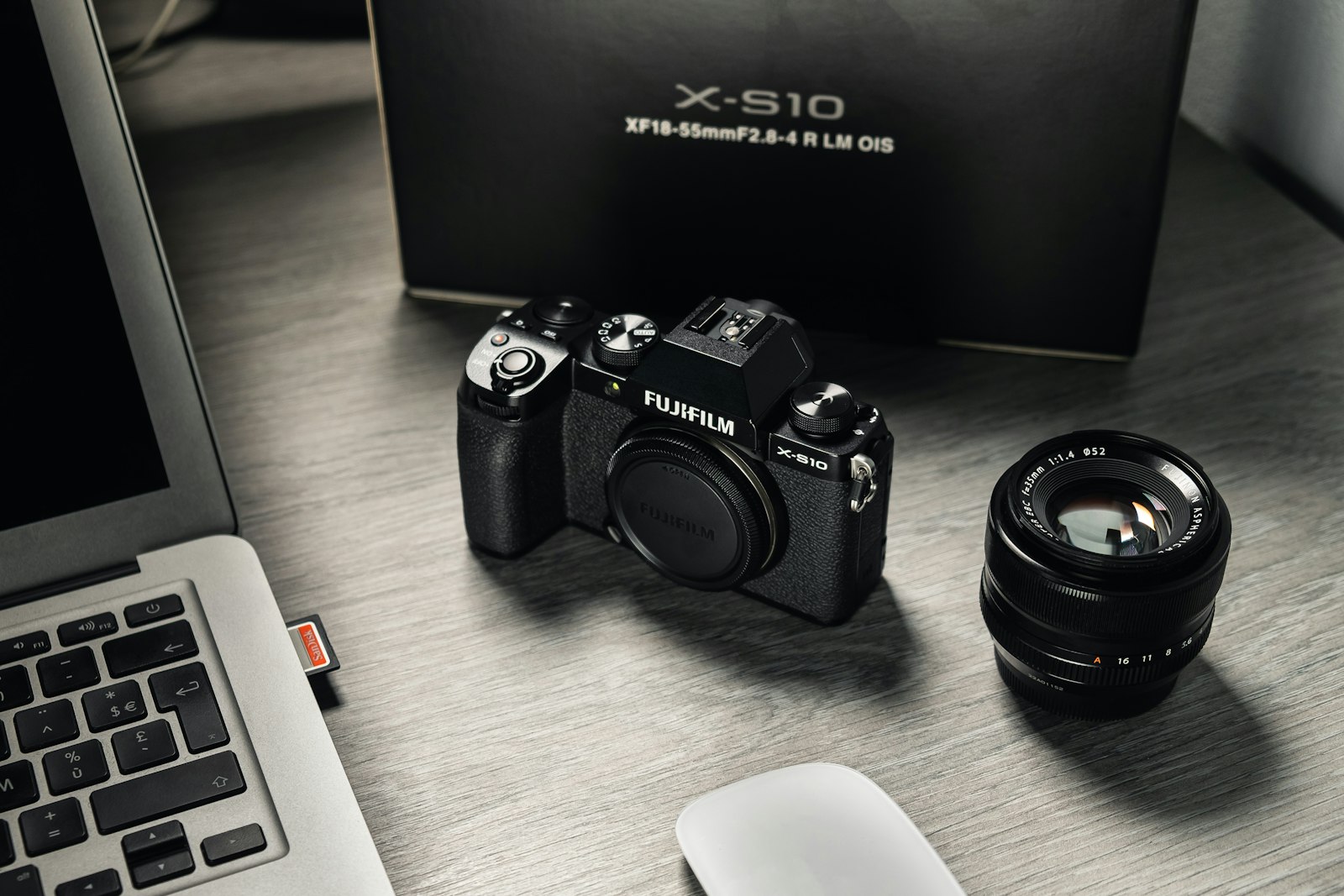 black mirrorless camera with a detached lens and its box beside a laptop on a desk