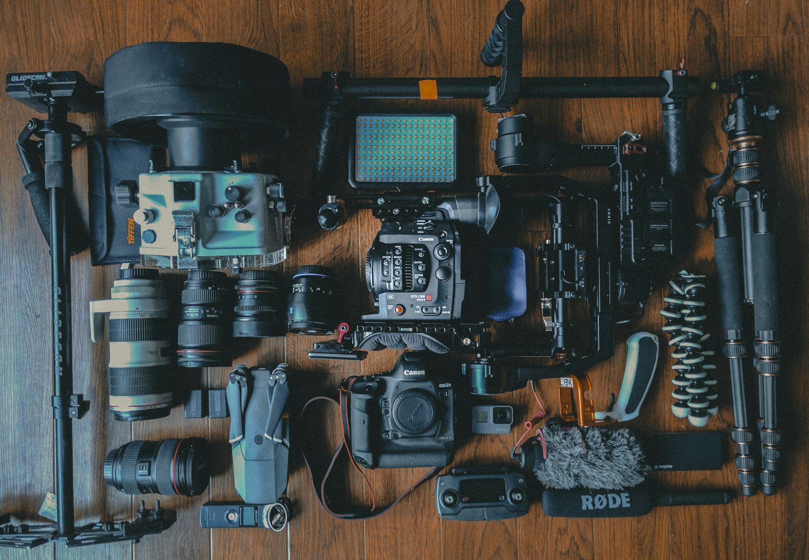 flat lay of modern camera bodies, lenses, tripod, and microphone on a wooden surface