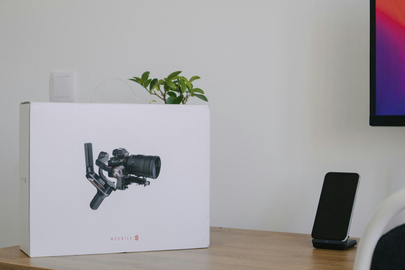 handheld gimbal-stabilized camera pictured on a white product box on a wooden desk