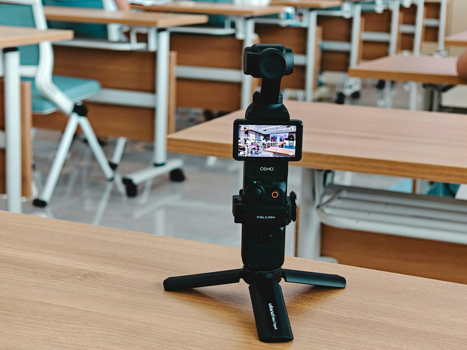 compact gimbal camera on a mini tripod with its screen open on a wooden table in a classroom