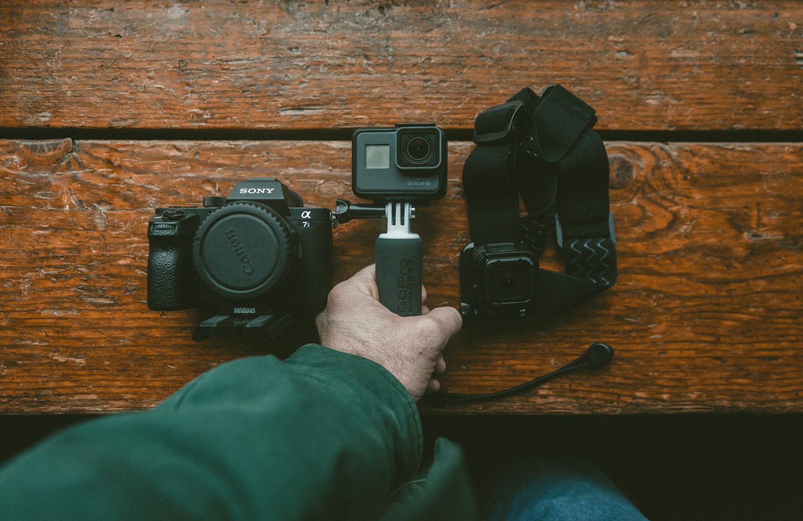 action camera and mirrorless camera body with mounts and straps on a wooden surface