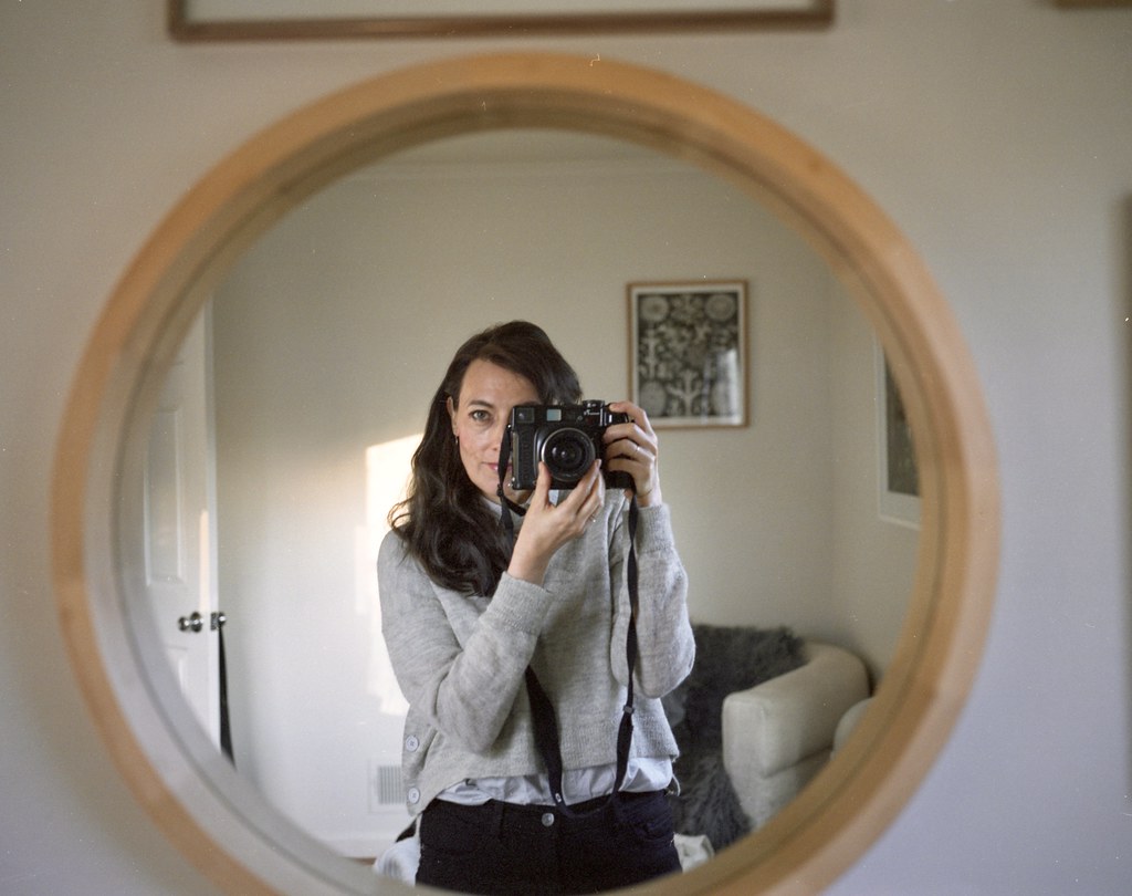 person holding a medium format film camera reflected in a round mirror