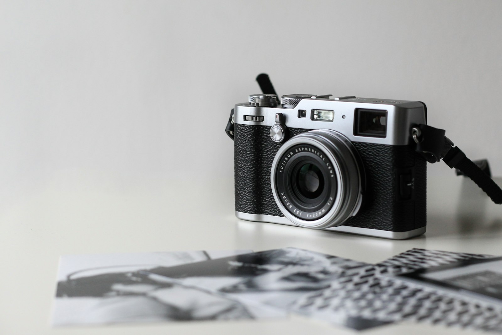 compact silver and black mirrorless camera beside printed photographs on a white surface