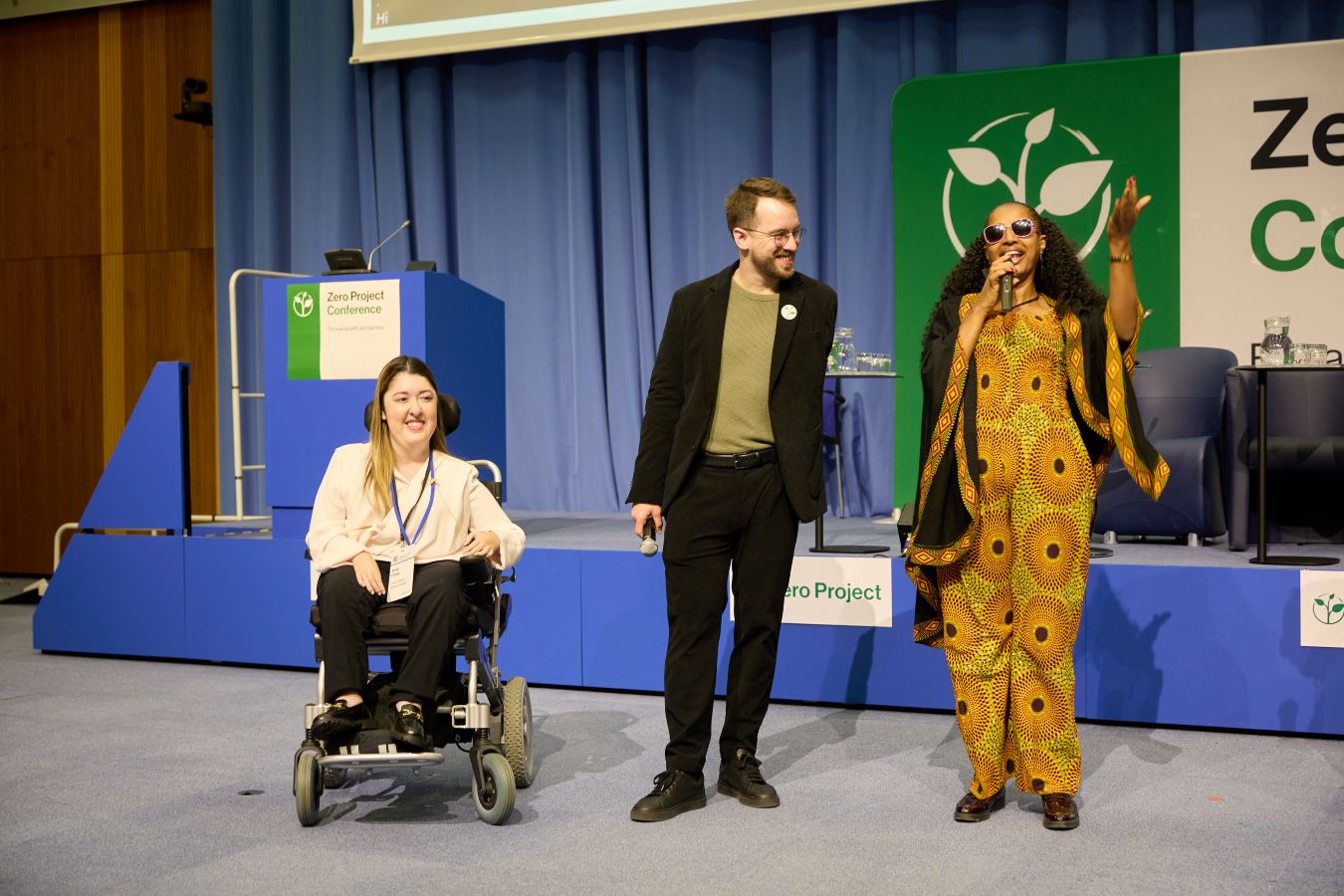 The three conference moderators standing next to each other at last year's conference; they are all smiling as Yetneberesh is speaking into the microphone