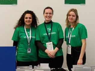 Three volunteers smile into the camera; they are all wearing Zero Project-green T-Shirts