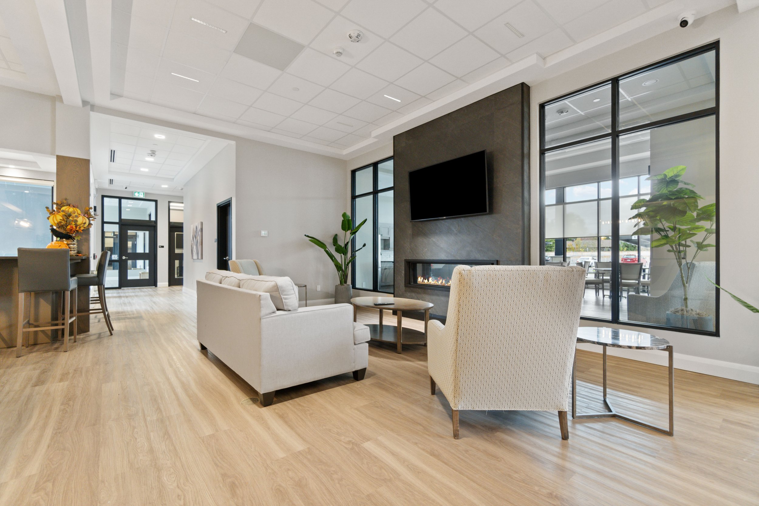 Modern lounge area with comfortable seating, a fireplace, large windows, and a flat-screen TV on the wall.