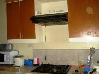 Kitchen with gas range and hood, rice dispenser, water kettle. There are cabinets with plates and kitchen utensils.