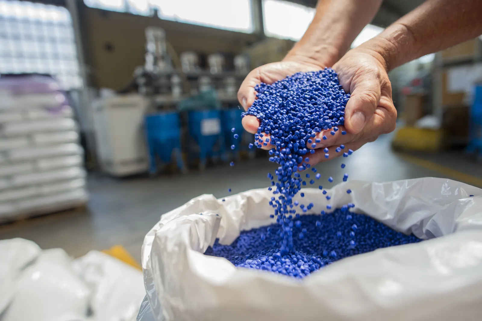 Pellet di plastica blu versati da mani in un sacco. Materia prima per la produzione industriale o il riciclo.