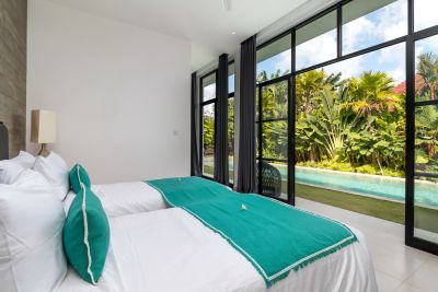 Modern tropical bedroom with white beds and green accents, large windows overlooking lush palms and infinity pool.