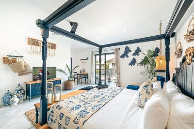 Cozy Balinese bedroom with black four-poster bed, tropical plants, woven decor, and poolside balcony view.