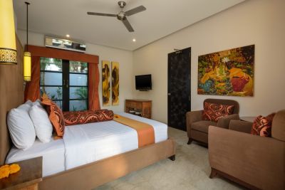 Luxurious Balinese bedroom with king bed, orange accents, ceiling fan, abstract wall art, and tropical garden views through sliding doors.