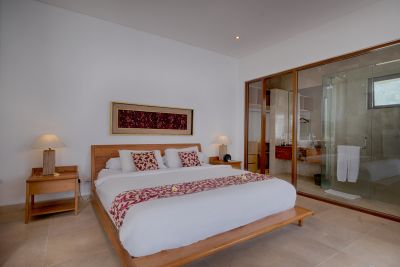 Modern tropical bedroom with low wooden platform bed, red floral bedding, bedside lamps, and open glass doors to en-suite shower.