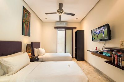Cozy twin bedroom in tropical style with two single beds, wall-mounted TV, ceiling fan, bookshelf, and balcony doors.
