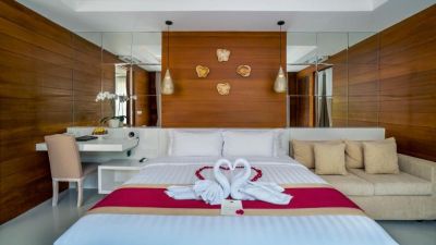 Luxurious Balinese-style hotel bedroom with wooden walls, king bed adorned with towel swans and rose, mirrors, desk, and orchids.