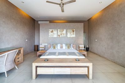 Modern minimalist bedroom with king-sized bed, wooden furniture, abstract art, and ceiling fan in neutral tones.