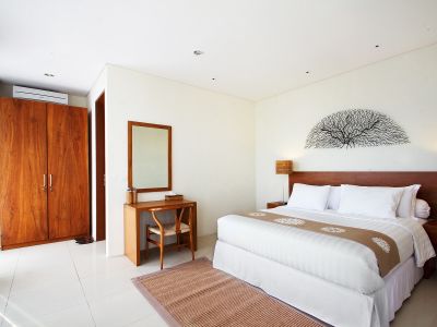 Spacious Balinese bedroom with wooden wardrobe, king bed, desk, mirror, and tree-branch wall art on white walls.
