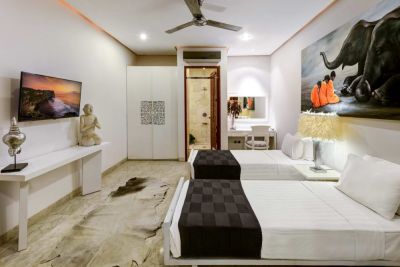 Spacious Balinese-style twin bedroom with white bedding, Buddha statue, elephant wall art, and ceiling fan.
