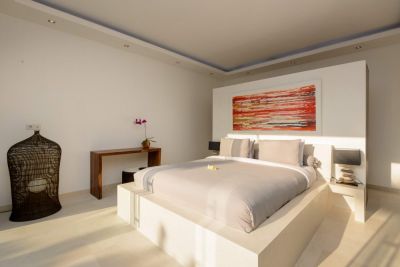 Modern minimalist bedroom with platform bed, abstract red wall art, orchid vase, and natural light.
