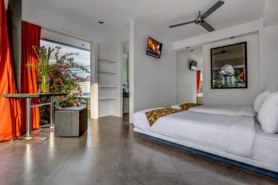Modern minimalist bedroom with a large white bed, red curtains, potted plants, ceiling fan, and tropical garden view through open doors.
