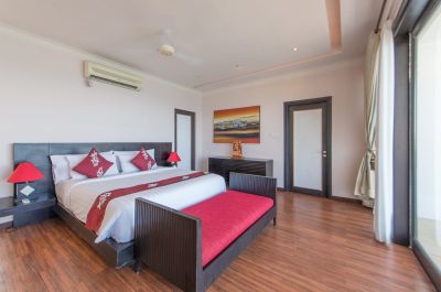 Luxurious Bali resort bedroom with king bed, red accents, ceiling fan, and panoramic ocean view through sliding doors.