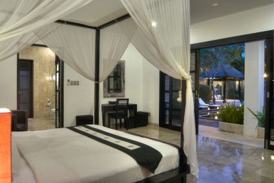 Elegant Balinese villa bedroom with white canopy bed, open doors to tropical poolside terrace at dusk.