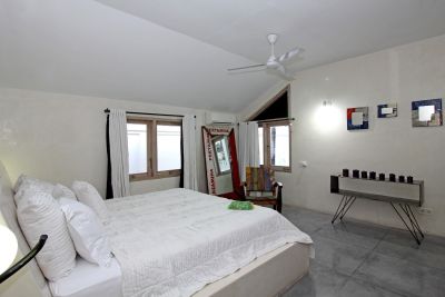 Modern minimalist white bedroom with plush bed, vanity mirror, ceiling fan, and abstract wall art.