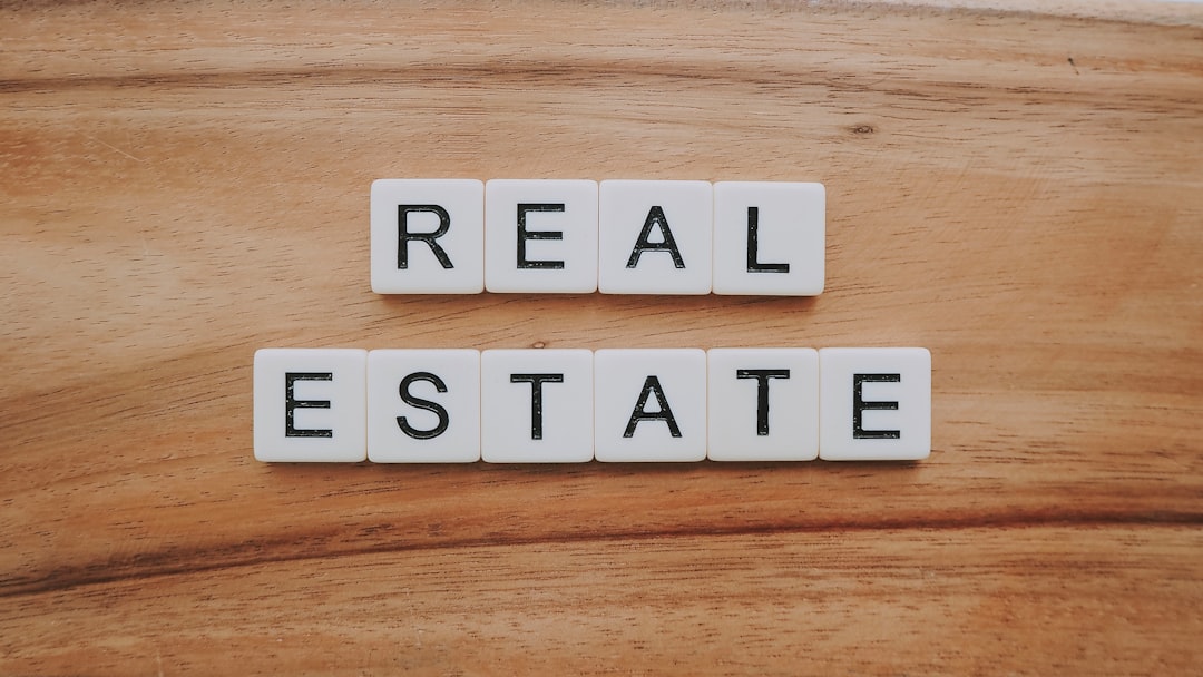 A close-up of wooden Scrabble-style tiles spelling out the words REAL ESTATE on a wooden surface.