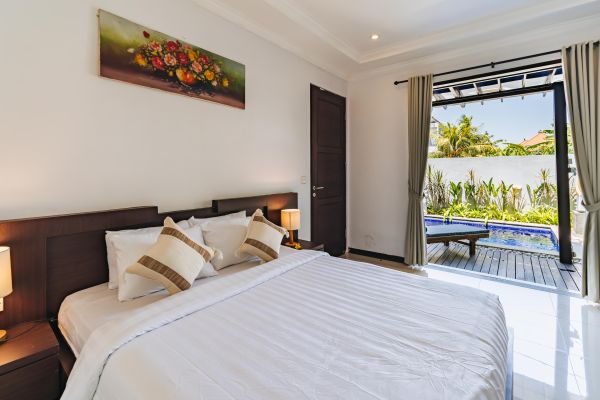 Spacious Balinese bedroom with king bed, open doors to private infinity pool, and tropical garden view.