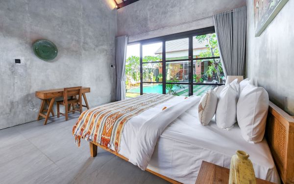 Spacious tropical bedroom with wooden bed and orange bedding, featuring large glass doors overlooking an infinity pool.