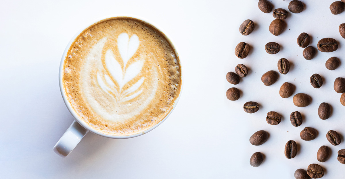 latte on a white table with coffee beans scattered to the right