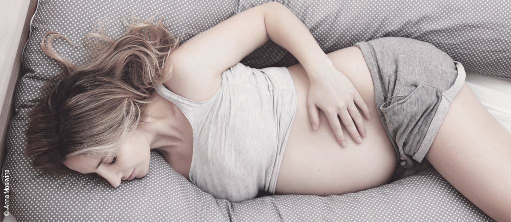 Foto: Eine Schwangere liegt in Seitenlage in einem sehr langen Seitenschläferkissen. 