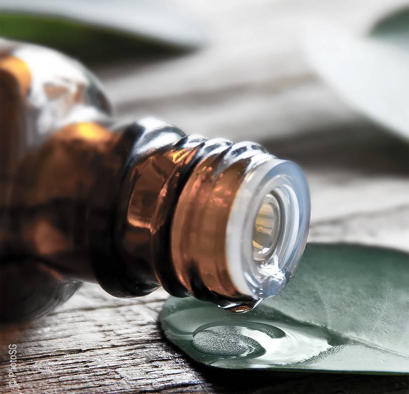 Foto: Eine Flasche Öl liegt umgekippt auf einem Holztisch. Einige Tropfen Öl tropfen auf ein Blatt.