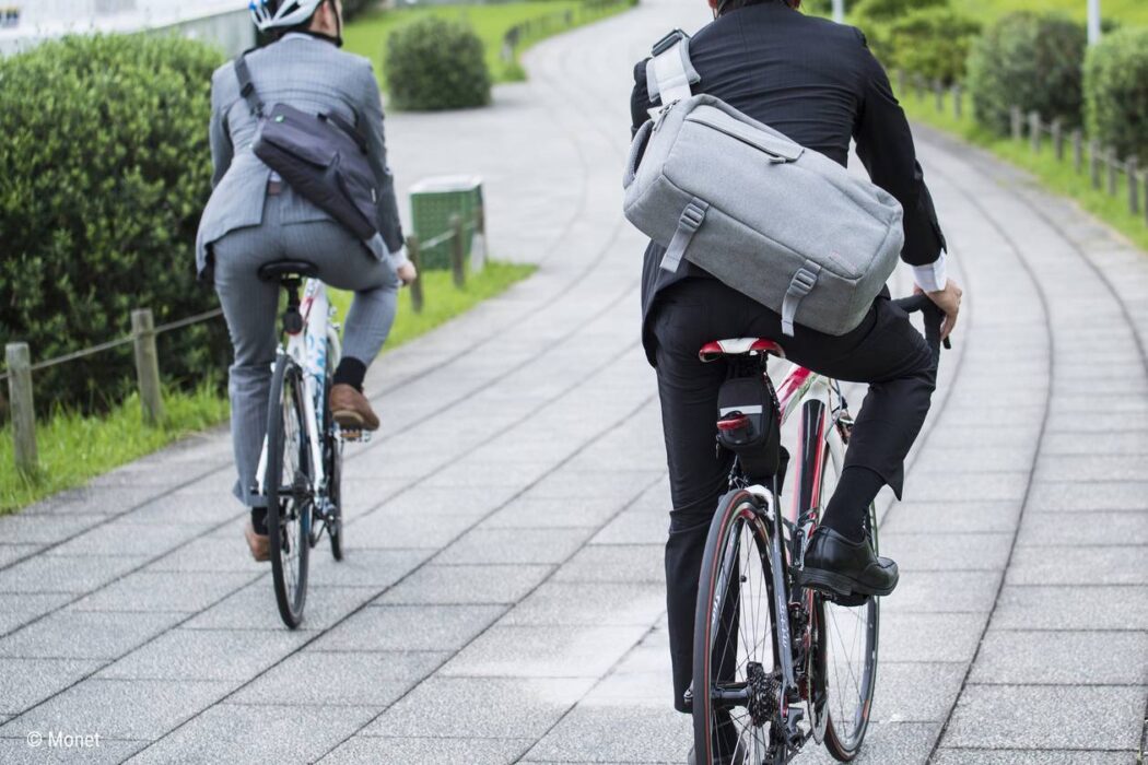 Foto: Zwei Radfahrer in Business-Anzügen auf einem breiten Radweg von hinten aufgenommen.