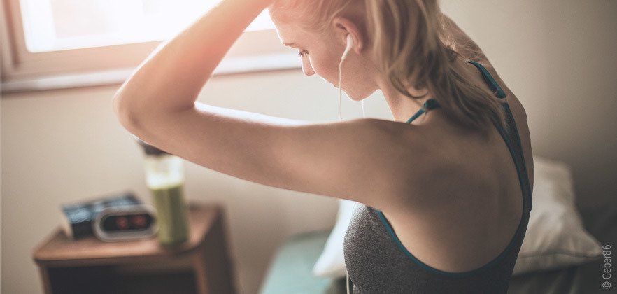 Foto: Ein Mensch sitzt in Sportbekleidung auf dem Bett und bindet sich die Haare zusammen. 