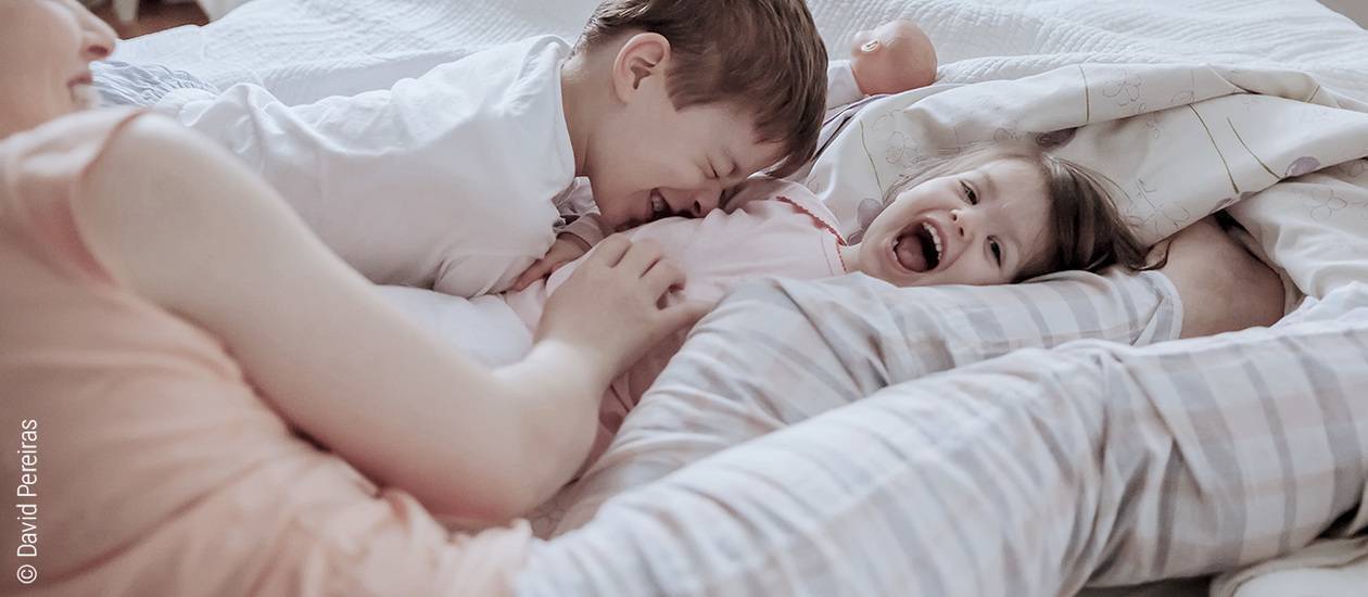 Foto: Eine Familie tobt und kuschelt gemeinsam im Bett.