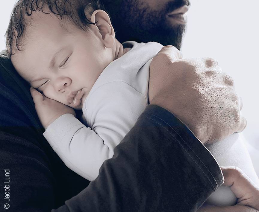 Foto: Ein Vater hält seinen Schlafenden Säugling im Arm.