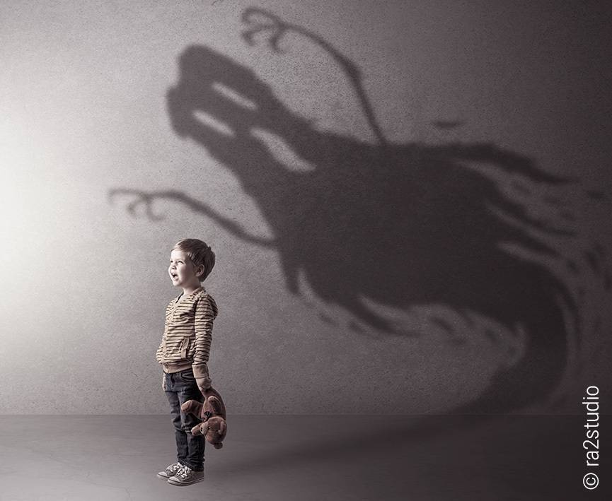 Foto: Ein kleiner Junge steht vor einer Wand. In seiner Hand hält er einen Teddybären. Hinter ihm ein düsterer Schatten in Form eines Gespensts