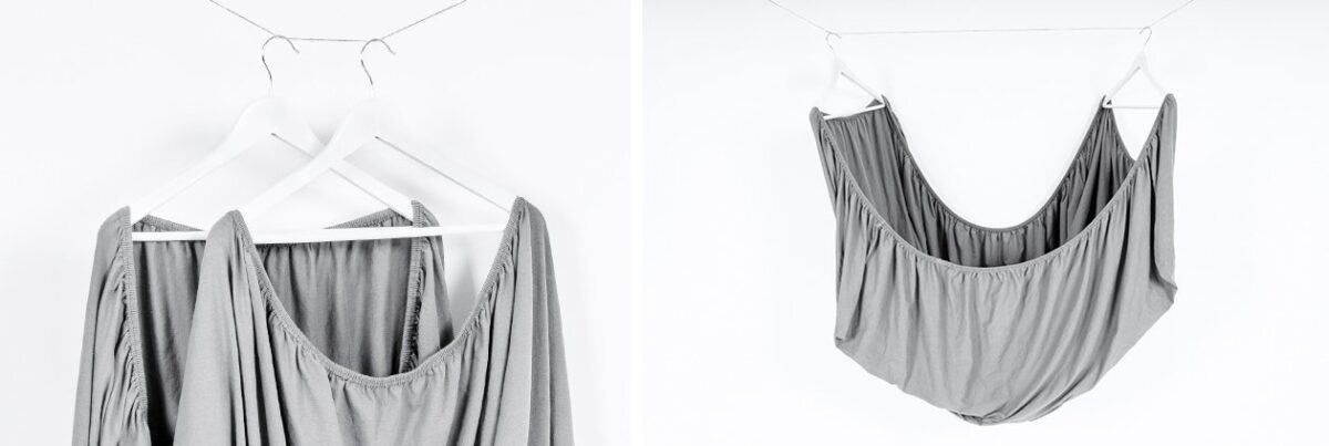 Foto: Ein Spannbettlaken ist zum schnelleren Trocknen auf zwei Kleiderbügel gehängt und leicht auseinandergezogen. Jeweils zwei Ecken befinden sich auf einem Bügel.