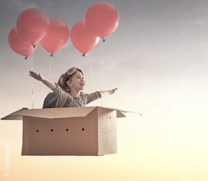 Illustration: Traumdeutung Fliegen – ein Kind fliegt in einem Umzugskarton an dem Luftballons angebracht sind.