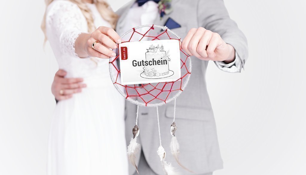 Foto: Ein Hochzeitspaar hält einen Traumfänger mit ausgestreckten Armen vor sich. Im Netz hängt der bett1.de Geschenkgutschein.