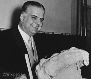 Foto: Der deutsche Chemiker Otto Bayer präsentiert seine Entdeckung von 1937, den Polyurethanschaum, im Jahr 1952; er steht vor einem Becher aus dem der Polyurethanschaum herausschäumt.