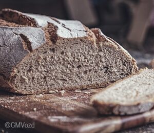 Foto: Ein typisch deutsches Mischbrot aufgeschnitten auf einem Holzbrett, davor eine einzelne Scheibe des Brotes. 