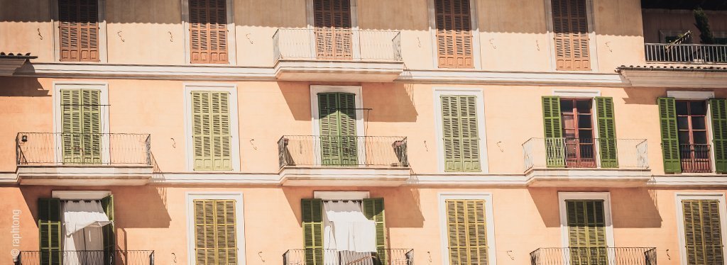 Foto: Die Sonne scheint auf ein südländisches Wohnhaus, bei dem die meisten Fensterläden geschlossen sind.