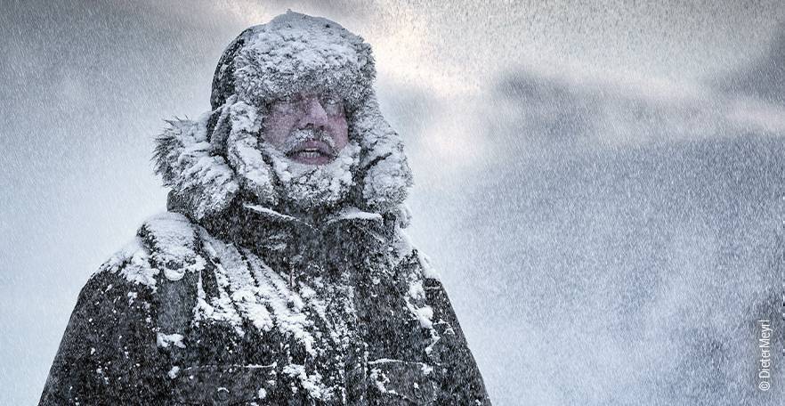 Foto: Ein Mann ist in dicker Winterjacke im Schneegestöber unterwegs.