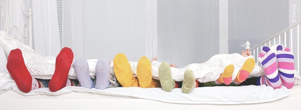 Foto: Sechs Menschen liegen in einem Bett, davon ein paar Kinder. Bunte Socken ragen aus der Bettdecke hervor.