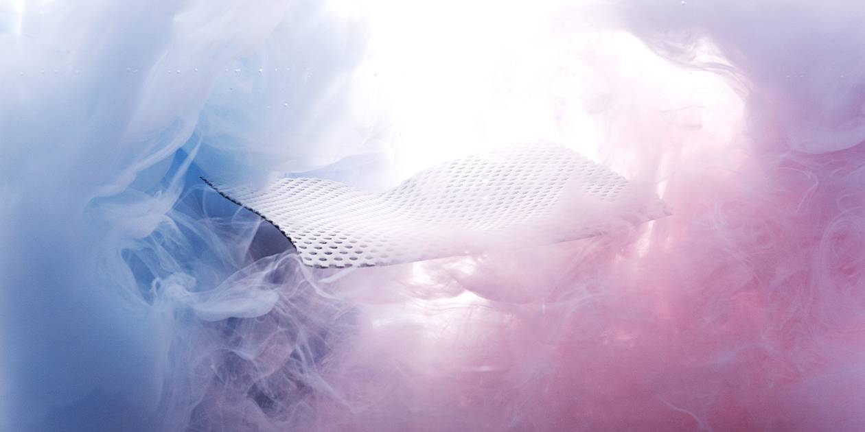 Unter Wasser: Ein Stück des HyBreeze Funktionsbezug schwebt in einer Art Wolke aus blauen und rosafarbenen Verwirbelungen